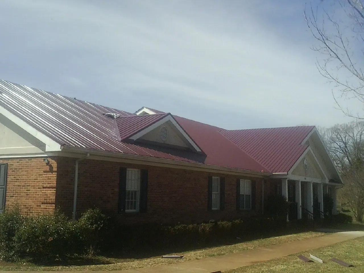 Red metal roof with gabled entries on a long brick building, from a Hail Damage Roof Repair job in Cordova